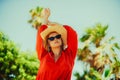 Fashion photo of a girl in black glasses with a chain and a large straw hat, a red dress on a background of palm trees. Wind in Royalty Free Stock Photo