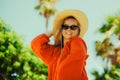 Fashion photo of a girl in black glasses with a chain and a large straw hat, a red dress on a background of palm trees. Wind in Royalty Free Stock Photo