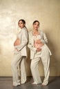 Fashion photo of two beautiful pregnant twins sisters posing together on the gold studio background