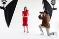 Fashion photoshoot. Professional photographer taking photos of female model in elegant red dress, posing in photo studio Royalty Free Stock Photo