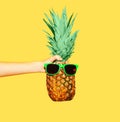 Fashion pineapple with sunglasses on yellow background, hand holding ananas