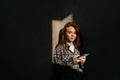 Fashion portrait of beautiful redhead young woman holding using mobile phone at shadow background in dark living room Royalty Free Stock Photo