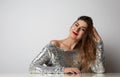 Fashion portrait of a beautiful smiling woman with long hair in a pretty silver dress with tinsel sitting at the table Royalty Free Stock Photo