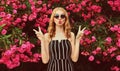 Fashion portrait beautiful young woman blowing red lips sending sweet air kiss over pink flowers Royalty Free Stock Photo