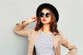 Fashion portrait beautiful young woman with red lips wearing black hat sunglasses coat over grey background Royalty Free Stock Photo