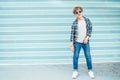 Fashion portrait of caucasian blonde hair 12 year old teenager boy dressed t-shirt and checkered shirt in blue sunglasses posing Royalty Free Stock Photo