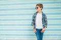 Fashion portrait of caucasian blonde hair 12 year old teenager boy dressed t-shirt and checkered shirt in blue sunglasses posing Royalty Free Stock Photo