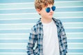 Fashion portrait of caucasian blonde hair 12 year old teenager boy dressed white t-shirt with checkered shirt in blue sunglasses Royalty Free Stock Photo