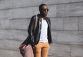 Fashion portrait elegant african man wearing a sunglasses and black rock leather jacket with bag in city, copy space empty Royalty Free Stock Photo