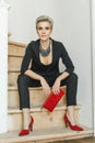 Fashion portrait of elegant woman with short haircut wearing black suit and red shoes with high heels holding red clutch. Studio Royalty Free Stock Photo