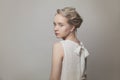 Fashion portrait of gentle young woman with blonde updo hair wearing white dress on gray banner background