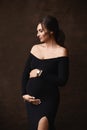 Fashion portrait of a gorgeous pregnant model girl wearing black evening dress posing over brown background