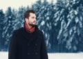 Fashion portrait handsome elegant bearded man wearing black coat in winter day over snowy trees forest background