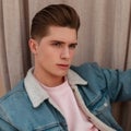 Fashion portrait handsome sexy young man with trendy hairstyle in stylish denim blue jacket with white collar posing outdoors Royalty Free Stock Photo