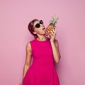 Fashion portrait of healthy woman biting pineapple over colorful pink background Royalty Free Stock Photo