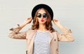 Fashion portrait pretty sweet young woman blowing red lips wearing a black hat sunglasses coat over grey