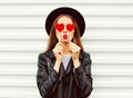 Fashion portrait pretty sweet young woman with red lips making air kiss with lollipop heart wearing black hat leather jacket Royalty Free Stock Photo