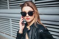 Fashion portrait pretty woman in black rock style in sunglasses using mobile phone over gray background in city Royalty Free Stock Photo