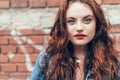 Fashion portrait of red curled long hair caucasian teen girl with applied red lipstick lips with blue eyes with a red brick wall Royalty Free Stock Photo