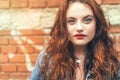 Fashion portrait of red curled long hair caucasian teen girl with applied red lipstick lips with blue eyes with a red brick wall Royalty Free Stock Photo