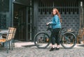 Fashion portrait of red curled long hair caucasian teen girl walking with bicycle on the city street. Natural people beauty urban