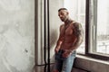 Fashion portrait of naked male model with tattoo and a black beard standing in hot pose on near the window. Loft room interio Royalty Free Stock Photo
