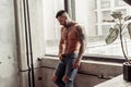 Fashion portrait of naked male model with tattoo and a black beard standing in hot pose on near the window. Loft room interio Royalty Free Stock Photo