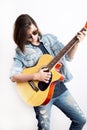 Fashion portrait of a teenager playing guitar in studio wearing sunglasses and jeans jacket Royalty Free Stock Photo