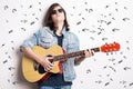 Fashion portrait of a teenager playing guitar in studio while wearing sunglasses and jeans jacket Royalty Free Stock Photo