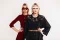 Fashion portrait two teenagers girlfriends in trendy colored youth sunglasses in red-black dresses near gray vintage wall. Comely Royalty Free Stock Photo