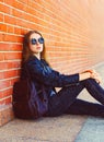 Fashion portrait woman in black rock style sitting over bricks background Royalty Free Stock Photo