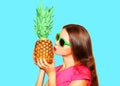 Fashion portrait woman kisses pineapple in sunglasses over blue