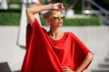 Fashion portrait of young pretty blonde girl in red dress and sunglasses. Beautiful woman model posing outdoor Royalty Free Stock Photo