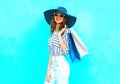 Fashion portrait young smiling woman wearing a shopping bags, straw hat, white pants over colorful blue background posing in city