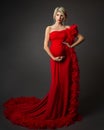 Fashion Pregnant Woman in Luxury Red Dress over Black. Elegant Mother embracing Belly in evening Gown with Feather. Pregnancy Royalty Free Stock Photo