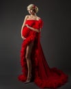 Fashion Pregnant Woman in Luxury Red Dress over Black. Elegant Mother embracing Belly in evening Gown with Feather. Pregnancy Royalty Free Stock Photo