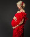 Fashion Pregnant Woman Side view Portrait in Red Dress over Black. Elegant Mother embracing Belly in Gown with evening Hairstyle. Royalty Free Stock Photo