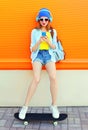 Fashion pretty cool girl listens to music using smartphone on skateboard over colorful orange Royalty Free Stock Photo