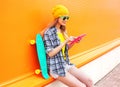 Fashion pretty cool girl using tablet pc with skateboard over colorful orange Royalty Free Stock Photo