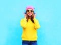 Fashion pretty cool smiling girl listening to music in headphones wearing colorful pink hat, yellow sunglasses and sweater Royalty Free Stock Photo