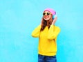 Fashion pretty cool smiling girl listening to music in headphones wearing colorful pink hat yellow sunglasses and sweater Royalty Free Stock Photo