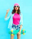 Fashion pretty cool woman in pink with skateboard over colorful blue Royalty Free Stock Photo