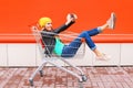 Fashion pretty cool young girl in trolley cart taking picture self portrait on smartphone wearing black jacket hat over colorful Royalty Free Stock Photo