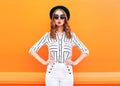 Fashion pretty glamour woman wearing a black hat sunglasses white pants over colorful orange