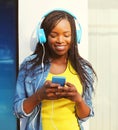 Fashion pretty smiling african woman in a headphones listens to music using smartphone in city Royalty Free Stock Photo