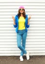 Fashion pretty smiling woman in colorful clothes posing over white background wearing pink hat yellow sunglasses and blue jacket Royalty Free Stock Photo