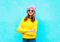 Fashion pretty smiling woman listening to music in headphones wearing a colorful pink hat, yellow sunglasses and sweater over blue Royalty Free Stock Photo