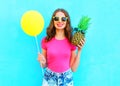 Fashion pretty smiling woman with yellow air balloon and pineapple wearing pink t-shirt over colorful blue background Royalty Free Stock Photo