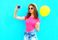 Fashion pretty smiling young woman taking picture self portrait on smartphone with yellow air balloon wearing a pink t-shirt Royalty Free Stock Photo