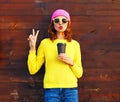 Fashion pretty woman with coffee cup in colorful clothes over wooden background wearing pink hat yellow sweater Royalty Free Stock Photo